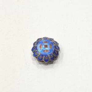 May include: A blue and gold enamel button with a geometric design. The button has a raised center with a square and four circles, all outlined in gold. The outer edge of the button is decorated with a row of gold dots.