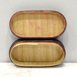 May include: Two oval-shaped, wooden boxes with black and brown trim. The boxes are made of woven bamboo and are stacked on top of each other.