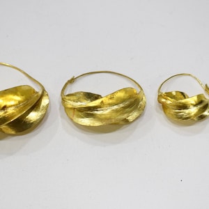 May include: Four gold hoop earrings with a twisted leaf design. The earrings are different sizes, with the largest being about 2 inches in diameter.