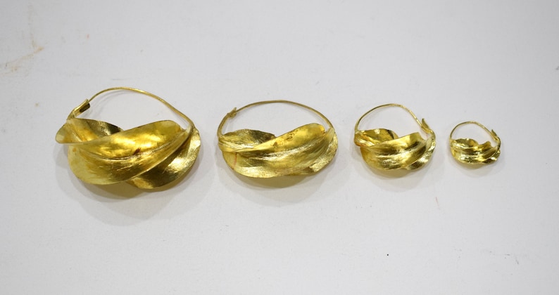 May include: Four gold hoop earrings with a twisted leaf design. The earrings are different sizes, with the largest being about 2 inches in diameter.