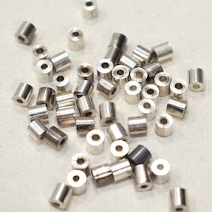 May include: A pile of silver metal jump rings, some are stacked on top of each other, on a white surface.