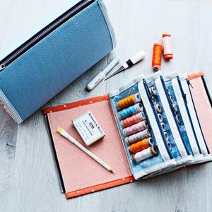 May include: A blue and orange sewing kit with a zipper, open to reveal spools of thread in various colors. The kit includes a box of pins, a pencil, and a pair of scissors. Additional spools of thread are also visible.
