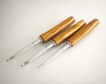 Può includere: Tre uncinetti con manici in legno e punte in metallo. Gli uncinetti sono etichettati F/5, G/6 e G/7.