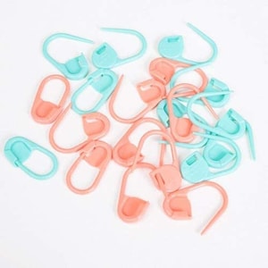 May include: A collection of plastic stitch markers in pink and blue. The markers are shaped like a loop with a small button on one end.