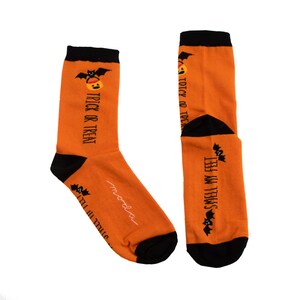 Könnte beinhalten: Ein Paar orangefarbene Socken mit schwarzem Besatz. Eine Socke hat den Text "Trick or Treat" und eine schwarze Fledermaus mit einem Kürbis. Die andere Socke hat den Text "Smell My Feet" und eine schwarze Fledermaus mit einem Kürbis.