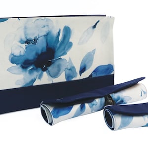 Peut inclure: Un ensemble de trois pochettes en tissu floral bleu et blanc avec une bordure bleu marine. Les pochettes sont enroulées et ont une fermeture à bouton.