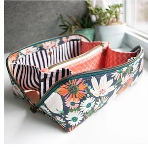 Könnte beinhalten: Geöffnete Kosmetiktasche mit einem Blumenmuster in Orange-, Weiß- und Rosatönen auf dunklem Blau. Der Innenraum hat gestreifte und korallenfarbene Fächer mit einem dunkelgrünen Reißverschluss.