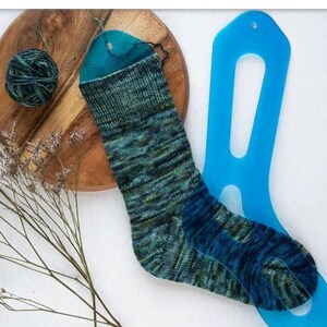 Op de afbeelding: Een blauwe en groene sok wordt over een blauwe plastic sokkenvormgereedschap gespannen. De sok is gebreid met een gemêleerd garen.