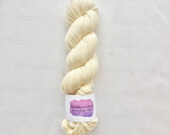 Może przedstawiać: Motka ręcznie farbowanej przędzy w kolorze kremowym z etykietą z napisem "Brediculous Hand Dyed Yarn".
