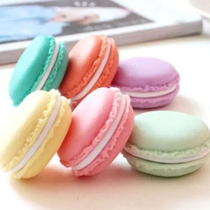 Puede incluir: Seis macarons de colores pastel con relleno blanco. Los macarons están dispuestos en semicírculo sobre una superficie blanca.