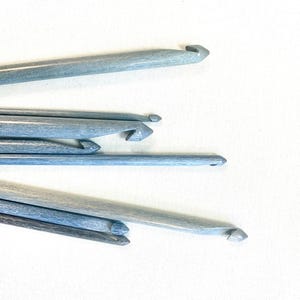 May include: A set of six wooden crochet hooks in various sizes. The hooks are a light blue color and have a smooth finish.