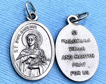 May include: Silver oval pendant with a depiction of Saint Philomena on one side and the text "ST PHILOMENA VIRGIN AND MARTYR PRAY FOR US" on the other side.