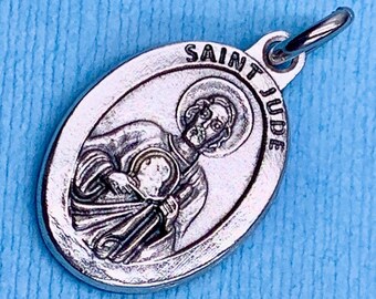 May include: Silver oval pendant with a depiction of Saint Jude Thaddeus, a Catholic saint. The pendant has the words "Saint Jude" inscribed around the edge.