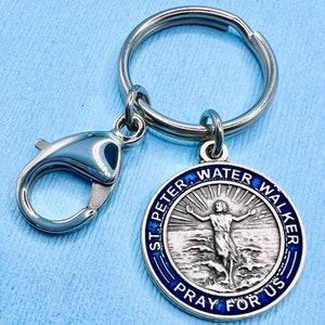 May include: Silver keychain with a blue enamel round charm featuring a depiction of Saint Peter walking on water. The charm has the text "St. Peter Water Walker Pray For Us" around the edge.