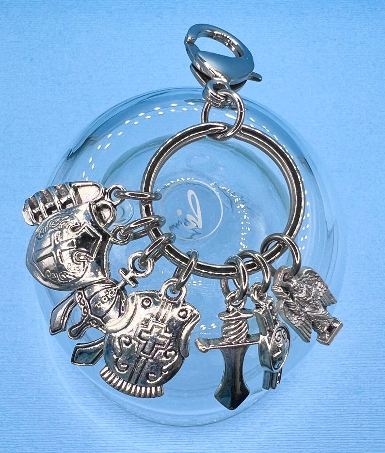 May include: Silver keychain with multiple charms, including a helmet, shield, sword, and eagle. The charms are attached to a silver ring and a silver clasp.