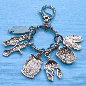 May include: Silver keychain with multiple charms, including a shield, a helmet, a lily pad, a cross, and a barrel. The charms are attached to a silver ring with a silver lobster clasp.