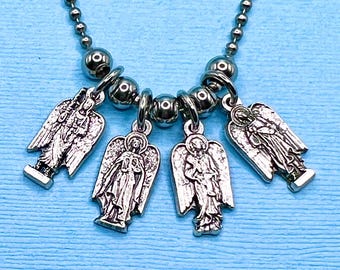 May include: A silver-toned necklace featuring four angel pendants. Each pendant is detailed with an angel figure and hangs from a silver ball chain. The necklace is displayed against a light blue background.