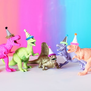 May include: Five colorful plastic dinosaur toys wearing party hats. The dinosaurs are pink, green, gold, purple, and orange.