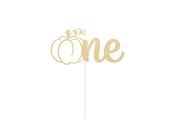 Peut inclure: Une décoration de gâteau à paillettes dorées représentant le contour d'une citrouille suivi du mot one en écriture cursive. Le motif est fixé sur une fine tige verticale blanche partant du bas du mot one pour insertion dans un gâteau.