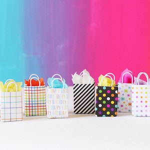 May include: A row of 12 colorful gift bags with various patterns, including polka dots, stripes, and plaid. The bags are arranged on a white surface in front of a rainbow-colored background.