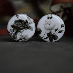 May include: Two round, white, glass cabochons with black and white floral designs. The cabochons feature a single rose with leaves and stems.