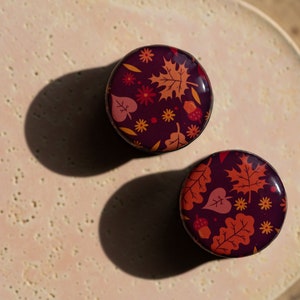 May include: Two round, purple containers with a fall-themed design. The containers feature a pattern of orange, red, and yellow leaves, acorns, and flowers.