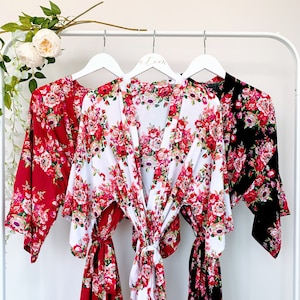 May include: Three floral print robes hanging on white hangers. The robes are in red, white, and black with a pink and green floral pattern.