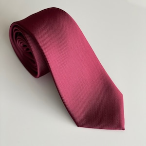 May include: A burgundy silk tie with a subtle ribbed texture. The tie is rolled up and ready to be worn.