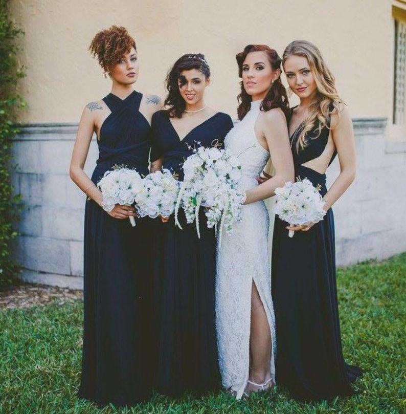 May include: Four bridesmaids in navy blue dresses holding white bouquets. The bride is wearing a white lace dress with a high neckline and a slit up the side.