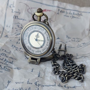 Pu&ograve; includere: Un orologio da tasca in ottone con una catena. Il quadrante dell'orologio ha uno sfondo bianco con una scritta nera che recita "2nd Breakfast C&eacute;a Dinner Lunch Afternoon".