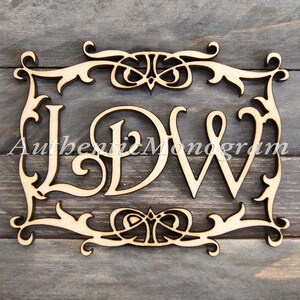 Op de afbeelding: Een houten monogram met de letters "LDW" in een decoratief frame. De letters zijn uit het hout gesneden en het frame heeft een bloemmotief.