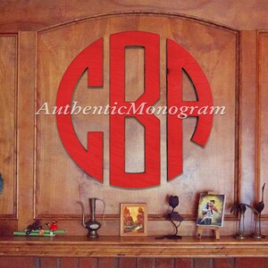 May include: A red wooden monogram featuring the letters "CBA" in a circular design, mounted on a wood panelled wall. The letters are cut out from the red wood, creating a negative space effect. The monogram is positioned centrally on the wall and is the main focus of the image. The text "AuthenticMonogram" is visible beneath the monogram.
