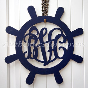May include: A navy blue wooden ship's wheel with a monogram of the letters "BFC" in the center. The wheel has eight spokes and is hanging from a hook.