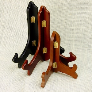 Puede incluir: Tres soportes de exhibición de madera con bisagras ajustables. Un soporte es negro y dos son de color marrón rojizo.