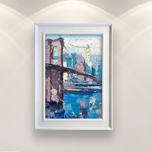A framed painting of the Brooklyn Bridge over a body of water with cityscape of New York in the background. The painting is done in a loose, impressionistic style with a palette of blues, purples, and browns.