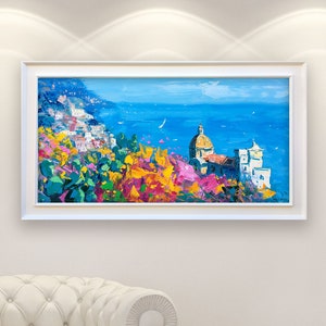 Panoramic Positano oil painting with church and flowers mounted in a white wooden frame in a modern home interior setting.