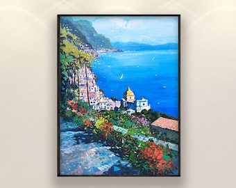 May include: A framed landscape painting depicts a coastal town with colorful buildings cascading down a hillside. The artwork features a vibrant blue sea, green mountains, and bright flowers, creating a scenic view. The painting is displayed on a white wall.