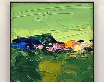 Puede incluir: Pintura de paisaje abstracto cuadrado con marco negro. La obra presenta un estilo texturizado, empastado, con tonos de verde, azul, amarillo y rosa. La pintura está montada en una pared blanca sobre un sofá blanco.