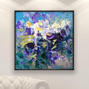 Square original oil painting with bold abstract purple and blue flowers, hanging above a white armchair near a large window in a modern living space.