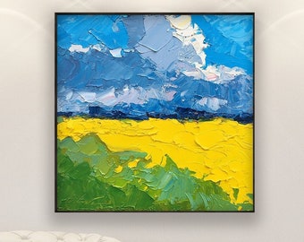 May include: Square abstract oil painting in a black frame. The artwork shows a landscape with a blue sky and clouds, a yellow field, and green grass. The painting is displayed on a white wall.