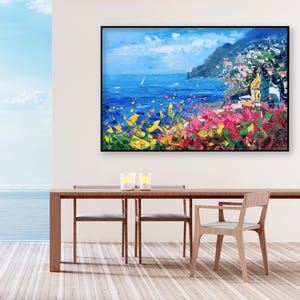 Original hand-painted oil painting on canvas depicting Positano on the Amalfi Coast, with colorful cliffside houses, deep blue sea, and vibrant Mediterranean flowers, framed and hanging on a bright dining room wall above a wooden table with sea view.