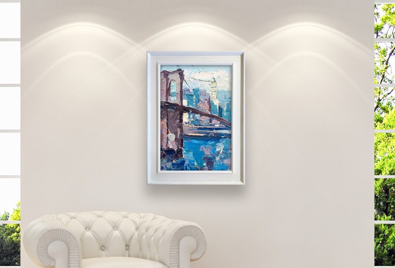 A framed painting of the Brooklyn Bridge over a body of water with cityscape of New York in the background. The painting is done in a loose, impressionistic style with a palette of blues, purples, and browns.