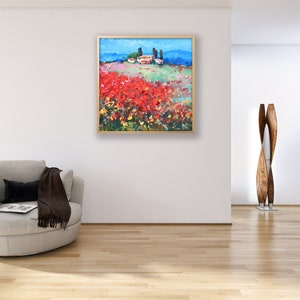 Puede incluir: Pintura de paisaje enmarcada que representa un campo de flores rojas bajo un cielo azul. A lo lejos, un pueblo con edificios blancos y &aacute;rboles verdes. La obra est&aacute; enmarcada en madera.
