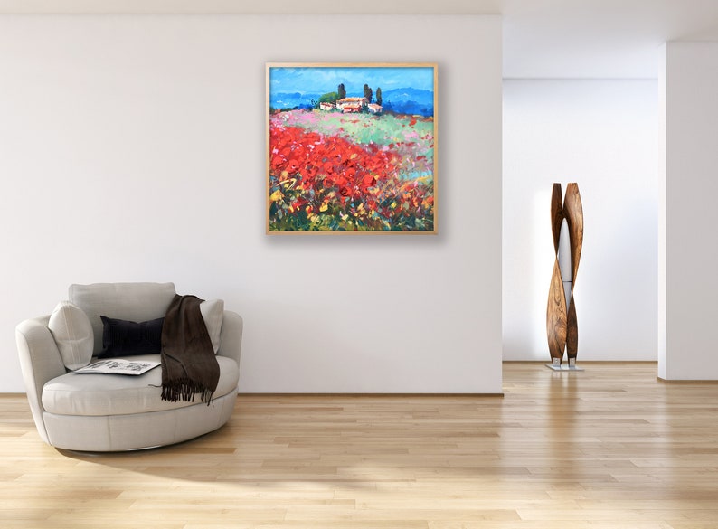 Puede incluir: Pintura de paisaje enmarcada que representa un campo de flores rojas bajo un cielo azul. A lo lejos, un pueblo con edificios blancos y &aacute;rboles verdes. La obra est&aacute; enmarcada en madera.