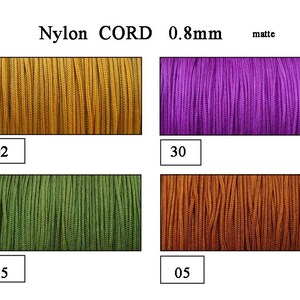Pode incluir: Quatro amostras de cordão de nylon fosco de 0,8 mm em diferentes cores: dourado, roxo, verde e marrom. O cordão é etiquetado como "Nylon CORD 0,8 mm fosco".