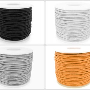 Puede incluir: Cuatro carretes de cordón elástico en negro, blanco, gris y naranja. El cordón está enrollado alrededor de un carrete de cartón blanco.