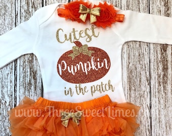 May include: Orange and gold baby outfit with a white long-sleeved bodysuit that says "Cutest Pumpkin in the patch". The outfit also includes a tulle skirt with a gold bow and a headband with a gold bow and orange flowers.