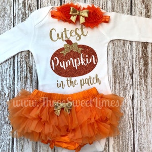 May include: Orange and gold baby outfit with a white long-sleeved bodysuit that says "Cutest Pumpkin in the patch". The outfit also includes a tulle skirt with a gold bow and a headband with a gold bow and orange flowers.