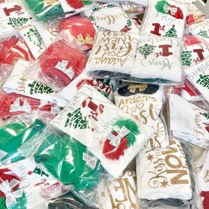 Puede incluir: Una pila de bodies blancos con varios dise&ntilde;os navide&ntilde;os y detalles de purpurina. Los bodies est&aacute;n empaquetados en bolsas de pl&aacute;stico transparentes. Algunos de los dise&ntilde;os incluyen "Arden's 1st Christmas", "Adaya's First New Year", "Kiss My  Mistletoe", y "Jerdyn's 1st Christmas".