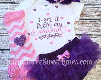May include: A baby outfit set with a white bodysuit, purple tulle bloomers, pink and white chevron leg warmers, and a purple headband with a pink bow. The bodysuit has the text "i get it from my mama" with pink and purple glitter hearts.